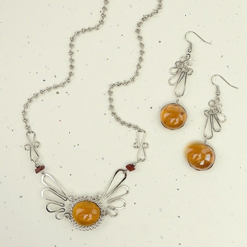 A picture of the alpaca mariposa set, A glass gem sit's in the middle of the necklace and earrings.