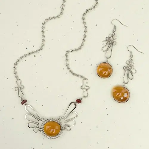 A picture of the alpaca mariposa set, A glass gem sit's in the middle of the necklace and earrings.