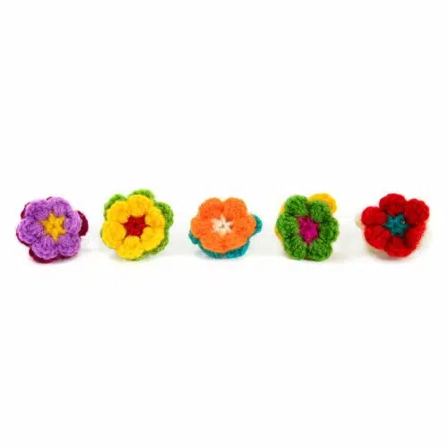 Five brightly colored rings that have hand crocheted flowers on top.