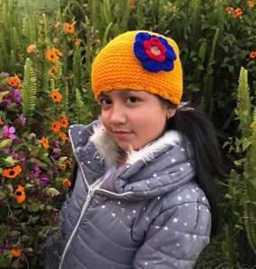 A kid showing off this brightly colored hat. The hat has a flower on top with scalloped edges of the hat