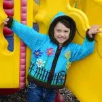 A young kid wearing the fenced garden sweater, comes in the color blue.