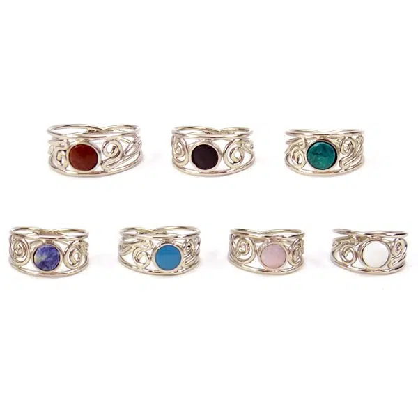 A picture of seven ornate stone rings, the colors of these rings are, red, brown, dark green, blue, turquoise, pink, and white.