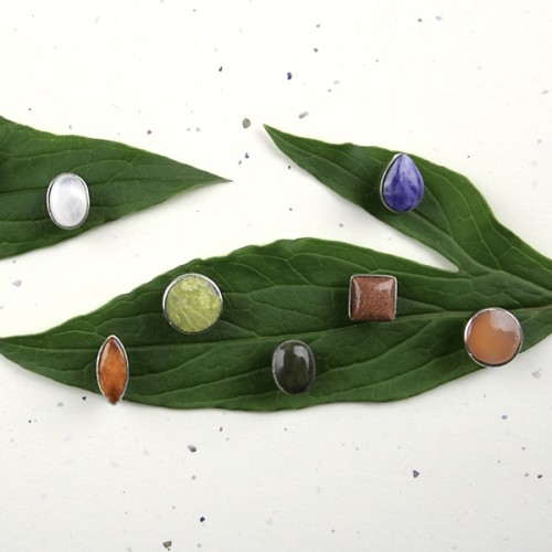 A picture of some fiori stud earrings, with some greenery in the back ground.