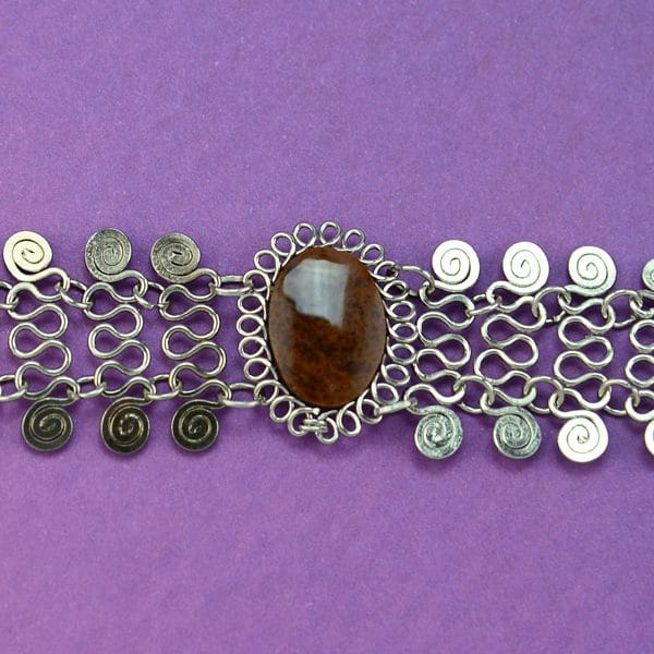A close up picture of the alpaca mesh necklace, has a semi precious stone in the middle, the color of the stone is brown.
