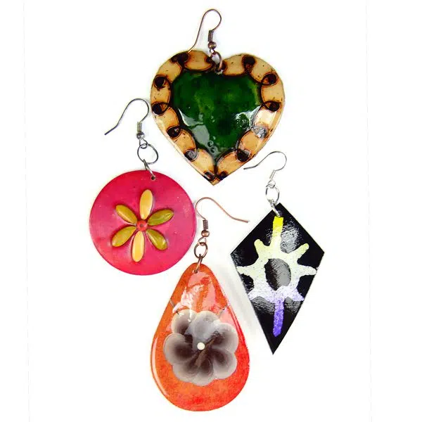 four different styles of the gourd diversity earrings, the four different styles are, A heart with a dark green center and a brown outline, a pink circle with some flower pedals in the middle, A black diamond, with a sun like design, and an oval with a flower in the middle.