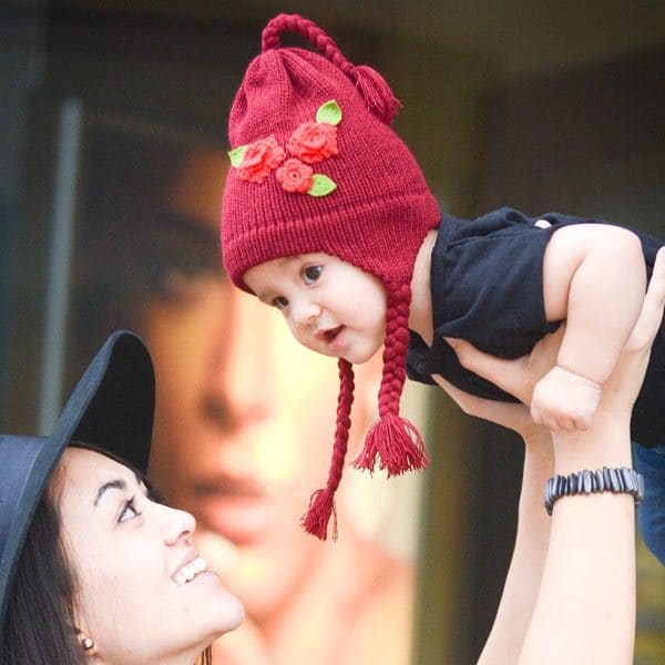 A young women holding up her kid in the air wearing the dark red hat with the bright red flowers on it