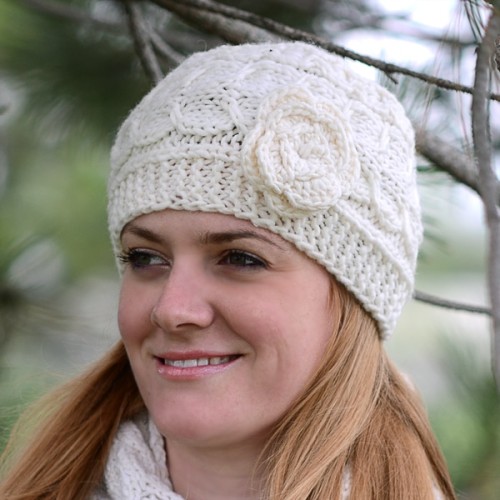 A young lady wearing A white hat with intricate knitting, and a flower on the side of the hat