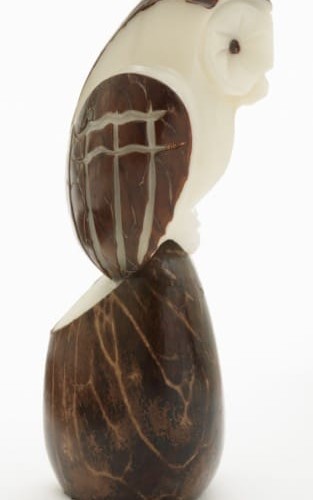 An owl sitting on a tagua seed, both are hand carved and made from tagua seeds