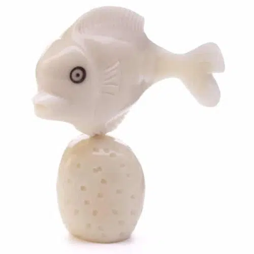 A fish sitting on top of a coral, made from a tagua seed.