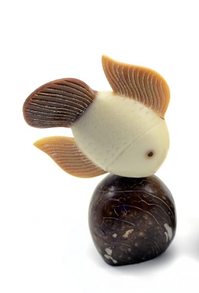A fish swimming downwards, towards a rock. made from a tagua seed.