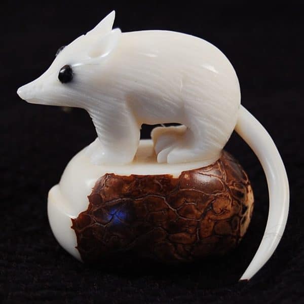 A hand carved mouse standing on a tagua seed