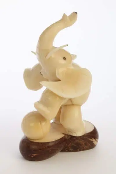 An elephant with a ball at its feet standing on a platform, made from tagua seeds