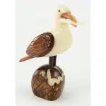 A seagull holding on to a fish while standing on a rock. hand carved out of tagua seeds