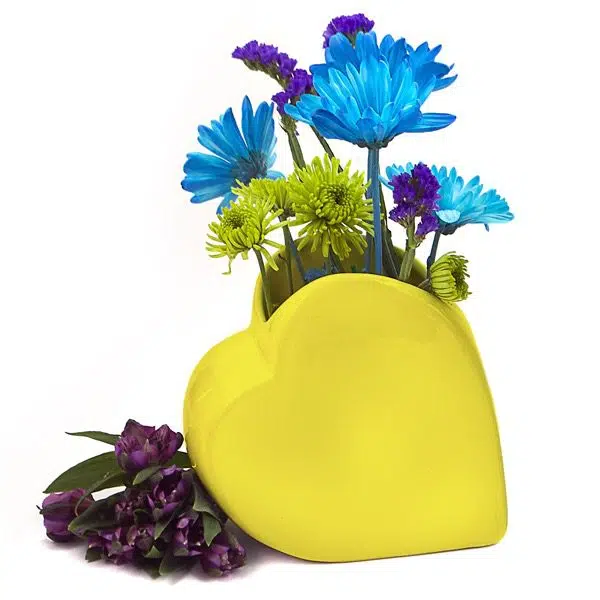 A yellow vase shaped like a heart, great for holding things. this vase is holding flowers.