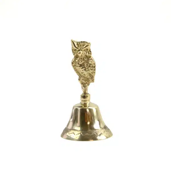 A captivating brass bell featuring an owl motif, photographed on a white surface.